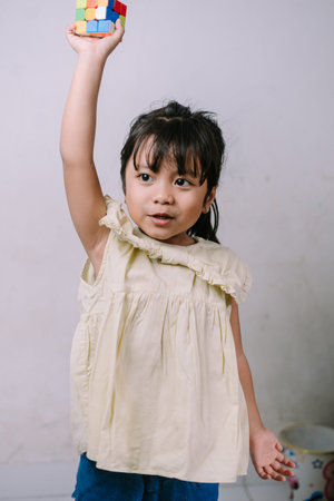 A bright young girl proudly holds a colorful problem-solving puzzle cube above her head, symbolizing...