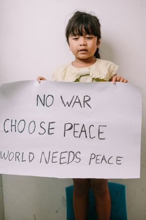 A young child stands holding a handmade sign advocating for peace and against war, expressing a...