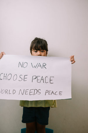 A young child holds a handmade sign with the powerful message 'NO WAR CHOOSE PEACE WORLD NEEDS...