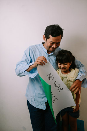 A smiling father and his young daughter are holding a sign that reads No War Peace, advocating for a...