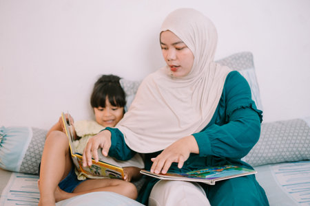 Loving Muslim mother sitting with her daughter while reading a colorful children's book, creating a warm and educational family moment.の写真素材