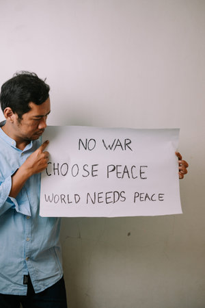 A man holds a powerful sign with the handwritten message 'No War, Choose Peace, World Needs Peace',...