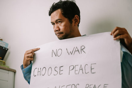 A man holds a protest sign displaying "NO WAR CHOOSE PEACE" against a plain white background, expressing his strong plea for global harmony and an end to conflict and violence.の写真素材