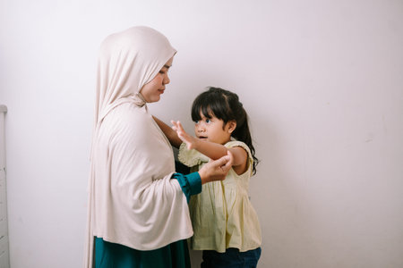 A loving Muslim mother wearing a hijab gently interacts with her young daughter at home. This...