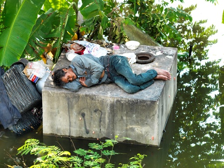 OCTOBER 21, Phathumtrani, Thailand  : homeless  man sleeping on concrete blog near streets of the city during the worst monsoon flood in  years のeditorial素材