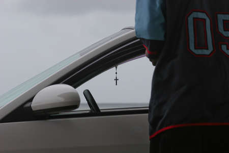 A scene depicting a modern car with a religios cross inside. The backside of a young man is visible. The scene express a contrast between urban life and religion.の写真素材