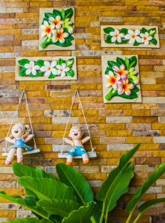 Plaster dolls of happiness children sitting on swing and plaster flower on the wall.の写真素材