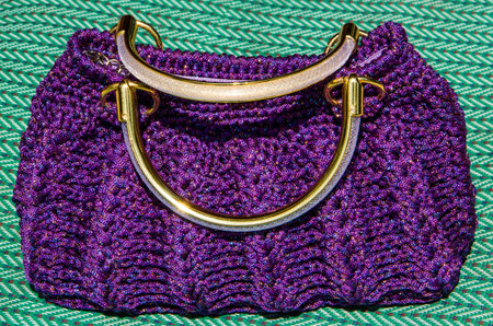 Purple crocheting hand bag on green mat.
