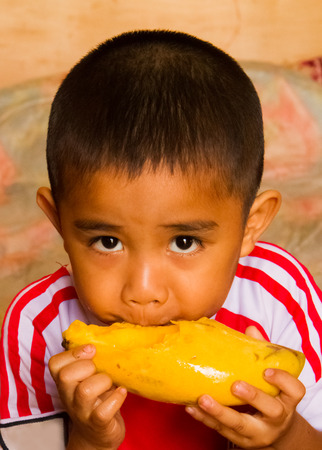 Asian boy eating yellow mango.の写真素材