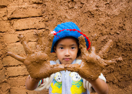 The girl with dirty hands while plastering earthen house.