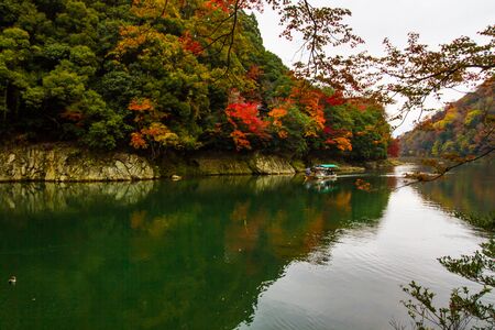KYOTO, JAPAN - NOVEMBER 25, 2019: Boatman punting the boat for tourists to enjoy the autumn view with maple trees along the bank of Katsura river in Arashiyama, Kyoto, Japan.Arashiyama is one of tourist destination in Kyoto.のeditorial素材