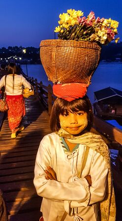 KANCHANABURI, THAILAND - DECEMBER 4, 2019 : The girl with flower basket on her head to sale for tourist on Mon bride at Sangkhlaburi in Kanchanaburi,Thailand.This bridge is the longest wooden bridge in Thailand.のeditorial素材