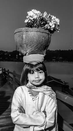 KHANCHANABURI,THAILAND-DECEMBER 4,2019: The girl with flower basket on her head to sale for tourist on Mon bride at Sangkhaburi in Kanchanabri,Thailand.This bridge is the longest wooden bridge in Thailand.のeditorial素材