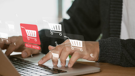 The idea of e-commerce or internet buying. A businessman uses a laptop to browse an online shopping basket. He buys and sells services across a network using global technology and the internet.の写真素材