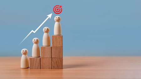 Teamwork and Leadership in Business Strategy. Wooden figures with happy faces stand on ascending blocks, with an arrow pointing to a target. growth, success, career advancement, and goal achievement.の写真素材