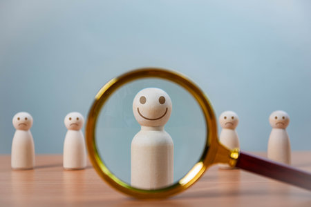 Leadership and Career Growth in HR. A magnifying glass focuses a smiling wooden figure among others, symbolizing talent selection, leadership, recruitment, personal growth, and individual recognition.の写真素材