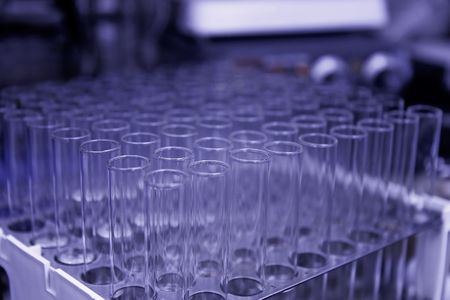Rack of test tubes set in front of a hot plate.  Shallow depth of field, low purple light, focus on the front test tubesの写真素材