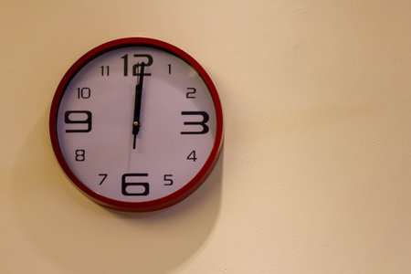 Modern looking wall clock showing 12AM/PM on a white background.