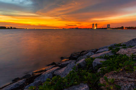 Rocky beach during sunset view with beautiful orange sky and building far away.の写真素材