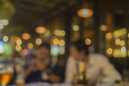 Blurred bokeh background with warm colorful lights of two man drinking in night club.の写真素材