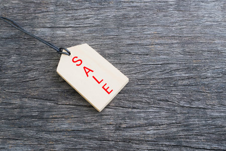 Red sale text on wood price tag on wood floor in background with copy space for some text,...