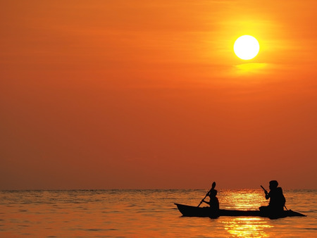 Blur defocus beautiful orange sky sunset above the sea with silhouette of man and boy paddle kayak in sea at Koh Kood, Thailand. Dramatic golden sky at the sunset background.の写真素材