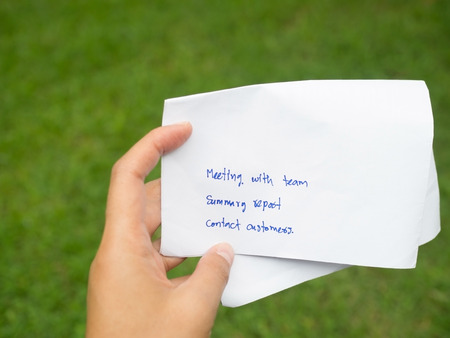 Woman hand holding white paper written day business plan. Meeting team, summary report and meet customers in green background. Business, daily plan, schedule and time management concept.の写真素材