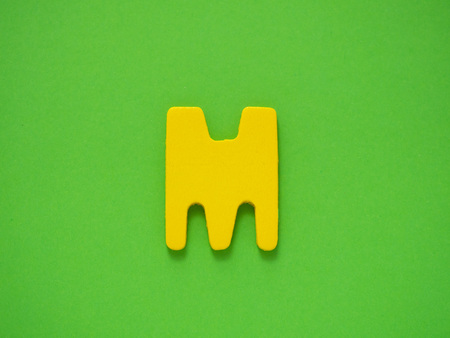Capital letter M. Yellow letter M from wood on green background.の写真素材