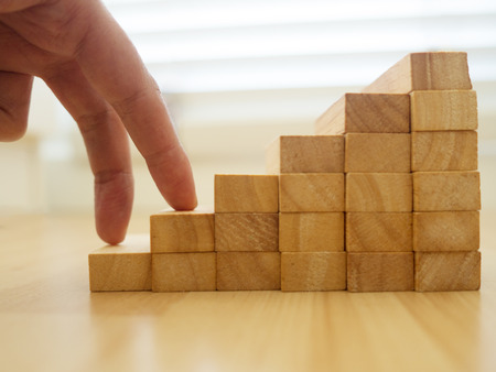 Woman fingers climbing on construction of wood block stacking as step stair on wood floor. Concept of growth success business.の写真素材