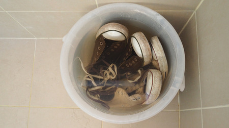 Old dirty black and white sneakers shoes with water in wash bucket.の写真素材