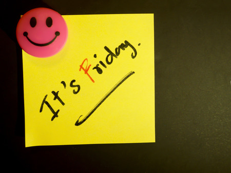 "It's Friday" hand writing text on yellow post it paper with pink smile magnetic on black background.の写真素材