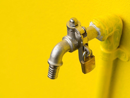 Yellow faucet on yellow wall with padlock prevent water theft. Concept of save water.の写真素材