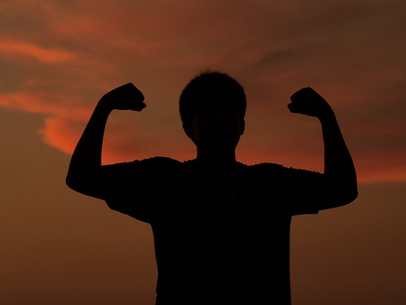 Silhouette successful winner young man gesturing raising arms at sunset against orange sky background.の写真素材