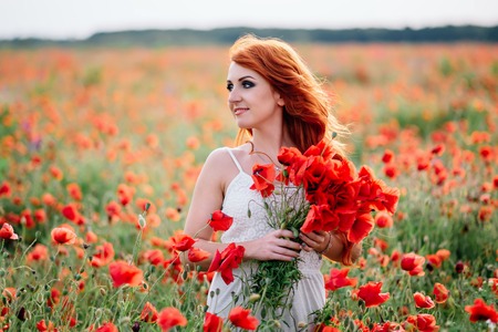 beautiful young woman in poppy field holding a bouquet of poppies, summerの写真素材