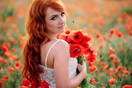 beautiful young woman in poppy field holding a bouquet of poppies, summerの写真素材