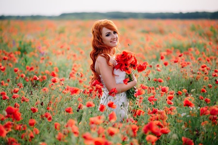 beautiful young woman in poppy field holding a bouquet of poppies, summerの写真素材