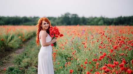 beautiful young woman in poppy field holding a bouquet of poppies, summerの写真素材