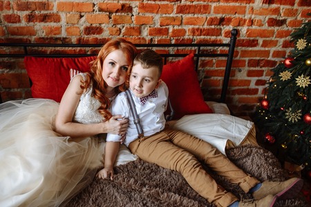 Christmas. Mother and son sitting on a bed in a room with a brick wall. Winter, new year.の写真素材