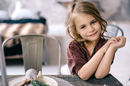 little girl sitting at a wooden table in the Marsala-colored dressの写真素材
