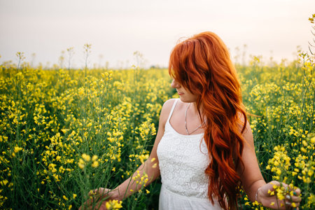 Young beautiful red-haired woman in a blooming rapeseed field at sunset