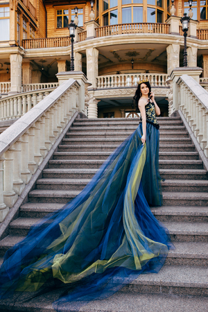 Young woman in a luxurious blue dress with a long train on the architecture backgroundの写真素材