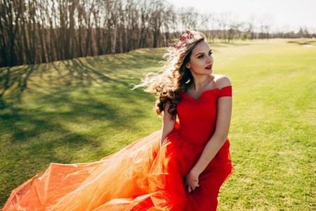 Young woman in a luxurious red dress with a long train On the green lawnの写真素材