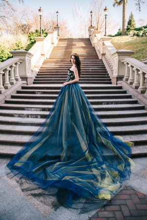 Young woman in a luxurious blue dress with a long train on the architecture backgroundの写真素材