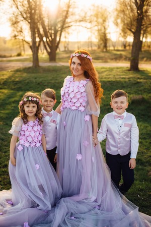 Young red-haired woman with her children in elegant clothes of purple hues hugging each other in the park at sunsetの写真素材