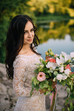 young bride stands on the river bank with a bouquet in her handsの写真素材