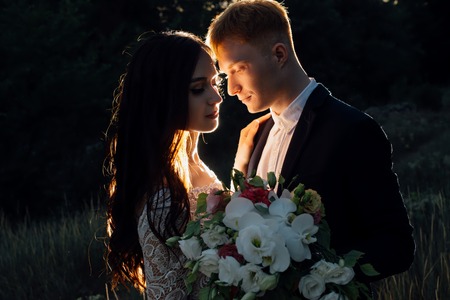 Newlyweds are standing and hugging outdoors, backlight, low keyの写真素材