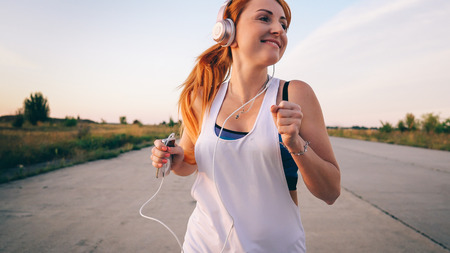 young woman runs and listens to music on headphones on a summer afternoon at sunsetの写真素材