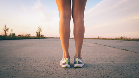 legs of a woman runner on the road close up at sunsetの写真素材
