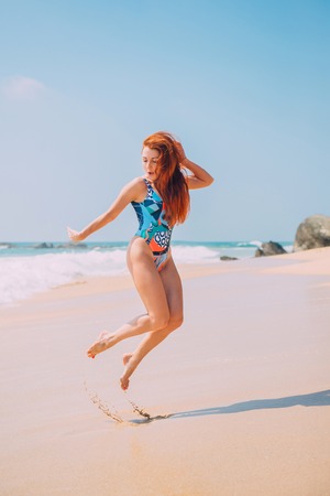 happy young red-haired woman jumping on a tropical beach on a sunny afternoonの写真素材