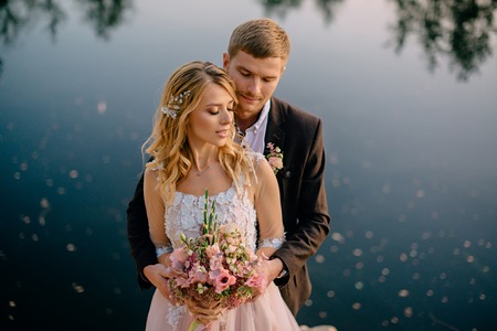 groom tenderly embraces the bride against the background of nature at sunset, close-upの写真素材